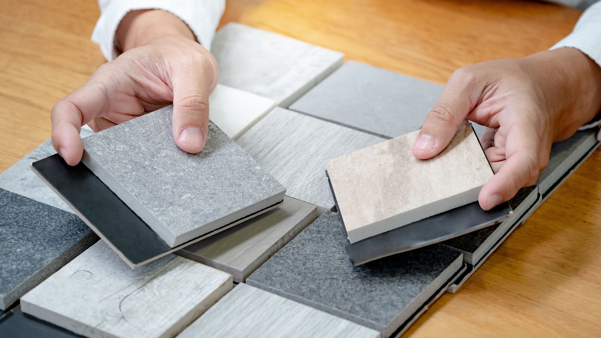 Architect hand choosing sample of stone material or tile texture collection on the table in studio. Designer working for interior architecture and furniture design project.